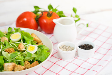 Fresh vegetable salad with fresh tomato, cucumber, lettuce, spinach, egg on plate topping with biscuits. There is a dressing in the small cup. Healty food concept