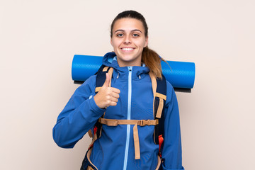 Young mountaineer girl with a big backpack over isolated background giving a thumbs up gesture