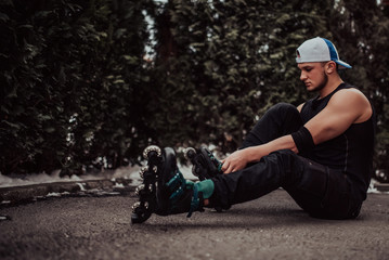 Attractive man sitting on a park putting on roller blades and prepares for a fun day skating