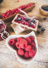 Bowl of raspberries with toast and spread jam on wooden table