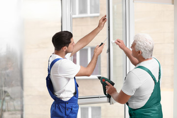 Fototapeta premium Construction workers repairing plastic window with screwdriver indoors