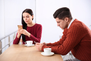 Couple addicted to smartphones ignoring each other in cafe. Relationship problems