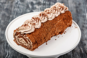 Chocolate biscuit roll with chocolate cream and cream decoration on a white stand