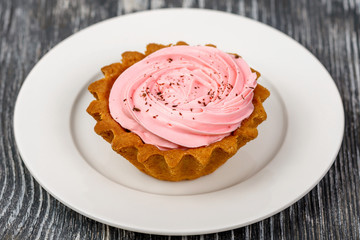 Cake basket with strawberry jam and pink cream on a white plate on a gray wooden table