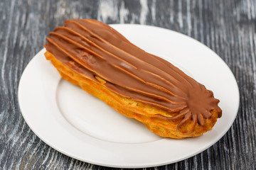 Cake eclair with chocolate cream and milk chocolate cap on a white plate