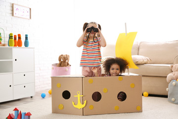 Cute little children playing with cardboard ship and binoculars at home
