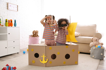 Cute little children playing with cardboard ship and binoculars at home