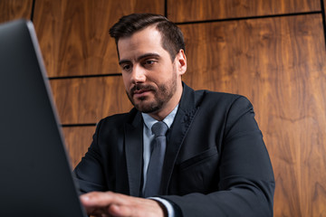 A good looking man in suit typing the contract on laptop. The concept of entering into legal power to take liabilities. Formal wearing.