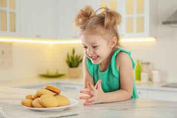 Cute little girl at table with cookies in kitchen