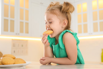 Cute little girl eating cookies in kitchen