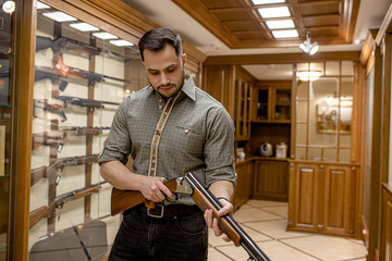 caucasian adult man reload a rifle for hunting in store, he stand with weapon around showcases....