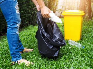 Asian women collect garbage in black bags, With yellow trash placed in garden. Cleanup and Take care of environment and preserve nature.