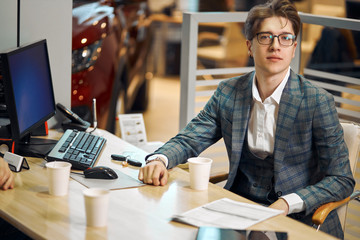 Fototapeta premium young successful handsome man in glasses sitting at workplace, close up photo. work, job, occupation, working hours. day, he is looking at the camera