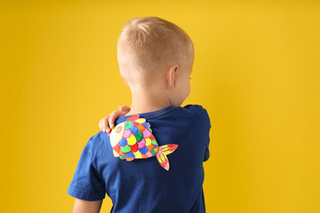 Little boy with paper fish on back against yellow background. April fool's day