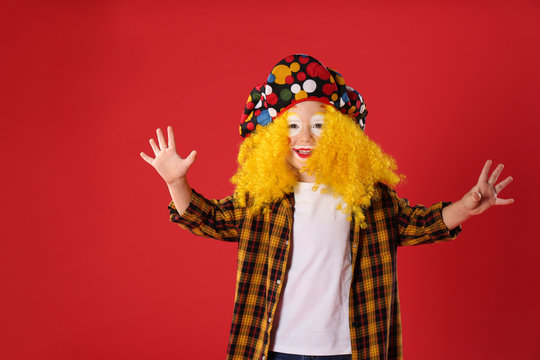 Funny little boy in clown costume on red background. April fool's day
