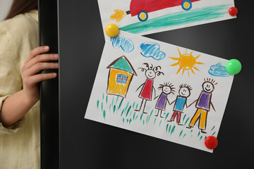 Woman opening refrigerator's door with drawings, closeup