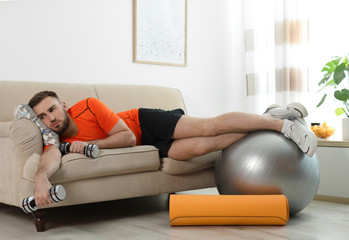 Lazy young man with sport equipment on sofa at home