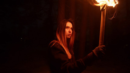 Young brunette woman traveler walking in the woods at night holding a torch