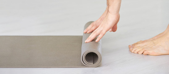 Yoga person rolling sport mat. Grey color. Gym carpet. Arms roll pad. Closeup concept with copyspace. Aerobics matt. Fitness club floor. Male nands. Teacher class background
