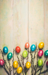 Easter festive background with soft focus with colored Easter eggs and willow twigs on wooden boards. Holiday decor. Warm retro toning. Top view, flat lay, copy space. Vertical orientation.