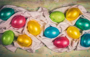 Creative Easter festive layout  with multicolored Easter eggs laid out on white textile napkin with pleats. Holiday decor. Warm toning. Retro toned image. Top view, flat lay.