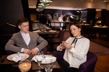 bad evening in a restaurant. young caucasian couple quarreled in representative luxury restaurant, woman use mobile phone while her boyfriend displeased with her behavior