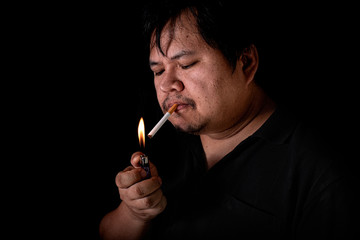 Fototapeta premium The fat man lighting up a joint with lighter smoking at the black background, Image of cigarette smoke spread in hand