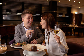 young caucasian married couple treating food with each other in restaurant. happy man and woman try delicious tasty food, dessert cooked by professional cook