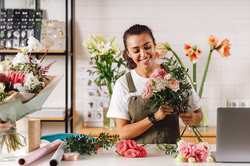 Happy female florist preparing a bouquet in her shop. Smiling woman holding flowers at counter.