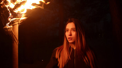 Young woman holding fire torch standing in dark forest