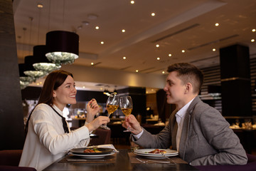 beautiful caucasian couple clink in restaurant. handsome guy and attractive lady sit and clink glasses in rich luxury restaurant, they drink champagne, have romantic date