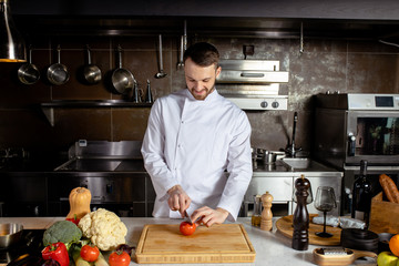 young professional cook man cut fresh vegetables in kitchen, he is cooking delicious garnish for clients in restaurant. culinary concept