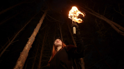 Young lost woman standing in scary winter forest at night with a handmade torch