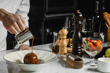 cropped professional cook pouring melted chocolate on sweet dessert. in restaurant
