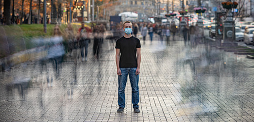 The man with medical face mask stands on the crowded urban street