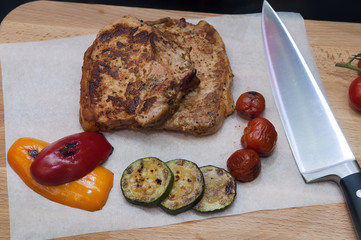 Grilled pork steak and baked vegetables on wooden board. Top view.