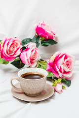 Fototapeta na wymiar Black coffee with pink roses on a white sheet