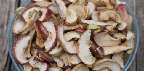 Background of dried homemade fruit Apple chips or slices in a glass plate on a wooden table. Health benefits of dried fruits, vegetarian food.