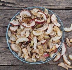 Background of dried homemade fruit Apple chips or slices in a glass plate on a wooden table. Health benefits of dried fruits, vegetarian food.