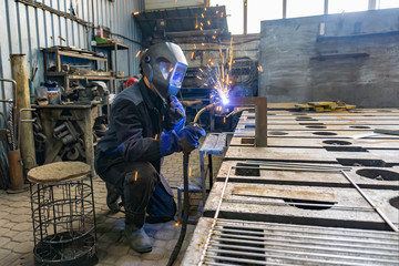 A welder in a workshop manufactures and connects metal structures, a worker in a protective mask performs welding work.