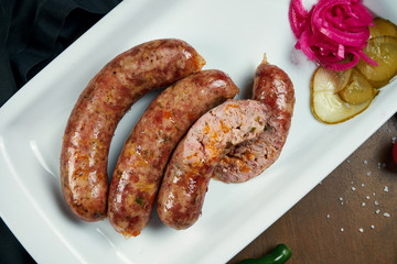Appetizing juicy pork minced sausage grilled in a smoker with cheddar in a white plate with canned vegetables. German beer snack