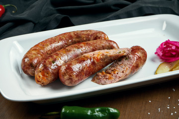 Appetizing juicy pork minced sausage grilled in a smoker with cheddar in a white plate with canned vegetables. German beer snack