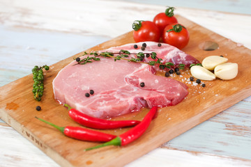 A pieces of fresh raw pork steak with tomatoes, thyme, pepper, red chili and galic on light wooden and on top with black pepper and salt. Raw pork is ready to cook. Food and kitchen concept