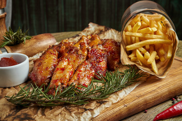Great beer snack - spicy baked buffalo wings. BBQ wings with garnish of french fries on a wooden...