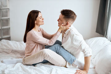 charming girl in beige sweater and jeans flirting with her handsome boyfriend wearing white shirt and pants, full length photo. side view