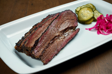 Close up view on tasty brisket beef from smoker on white plate on wooden background. Grilled meat pastrami