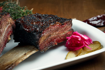Close up view on delicious appetizing smoked and grilled beef ribs. Barbecue ribs - a classic dish of American cuisine on a white plate. Selective focus