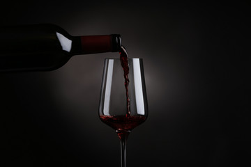 Pouring red wine from bottle into glass on black background