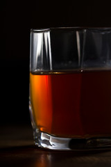 A glass of whiskey on a wooden table, close up . Low key style .