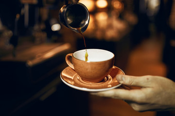 barista holding a cup with source pouring coffee in steel cup, close up cropped photo.good morning